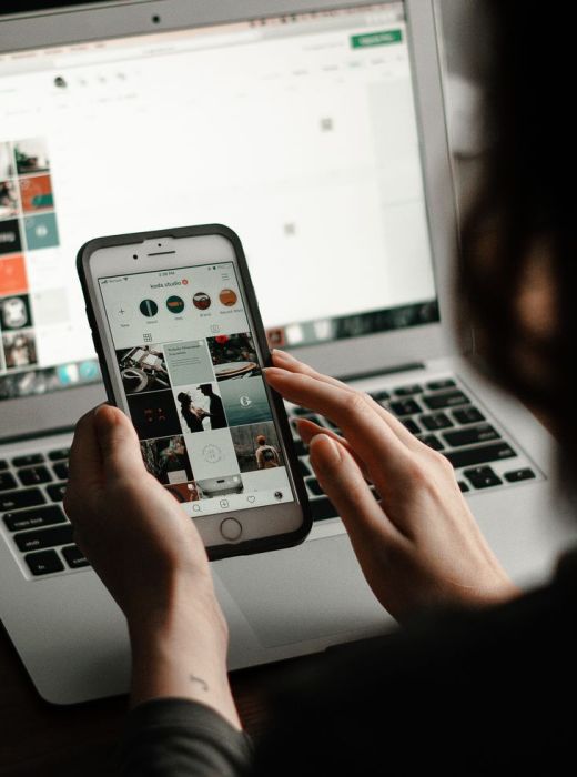 Woman holding mobile phone with social media content being viewed, and a laptop in the background with Las Vegas social media management services on the screen.
